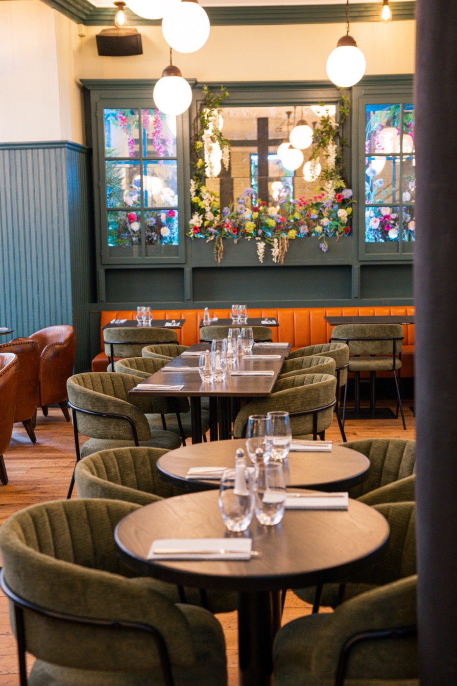 Orange banquette and laid tables under the flowered cabinets, Bistrot Jad