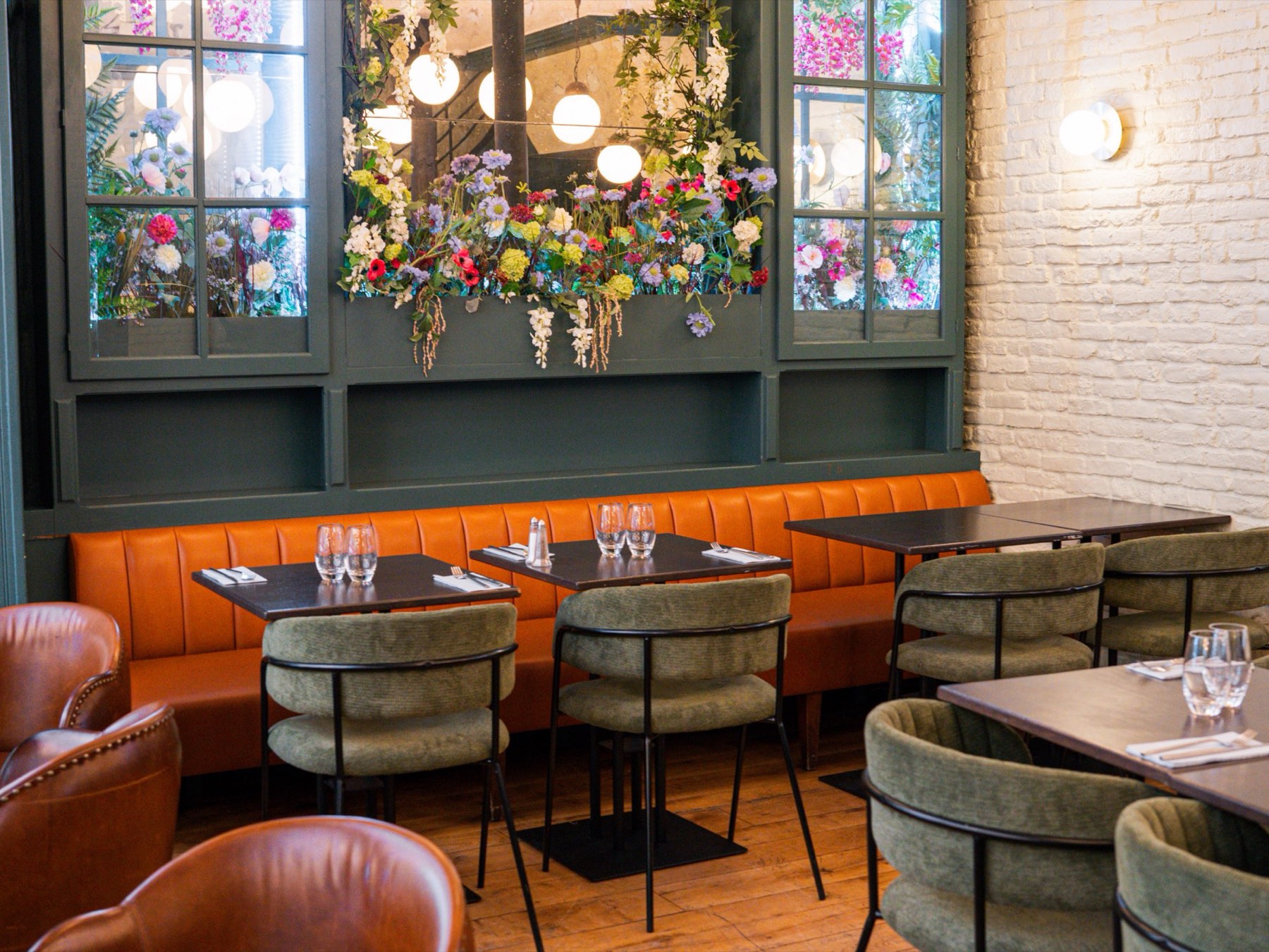 The dining room at Bistrot Jad: green flowered cabinets, an orange banquette and cognac leather armchairs
