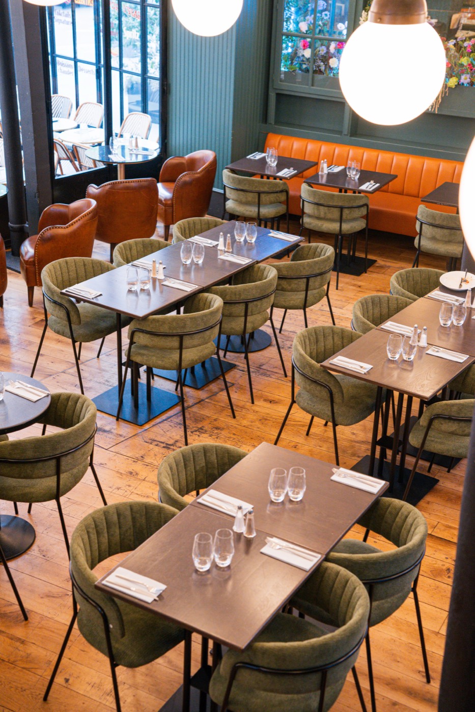The dining room at Bistrot Jad from above: green velvet chairs, an orange banquette and oak parquet